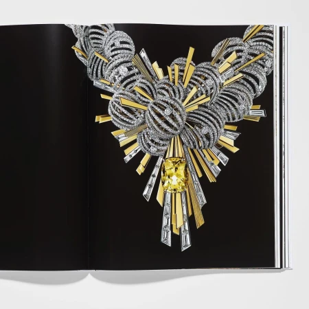 Intricate silver and gold necklace with yellow gem on black book page, luxurious jewelry design, high-fashion editorial, studio lighting.