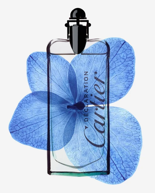 Elegant product shot of Cartier Declaration fragrance bottle with geometric cap, partially obscured by a blue hydrangea bloom on white.
