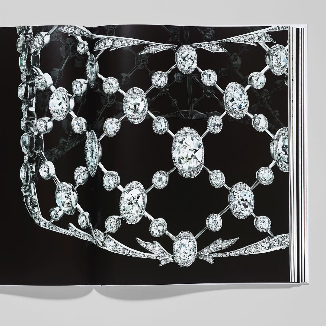 Close-up studio shot of a book open to a page featuring an elaborate diamond necklace and jewelry piece against a black background.