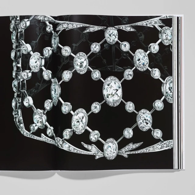 Close-up studio shot of a book open to a page featuring an elaborate diamond necklace and jewelry piece against a black background.