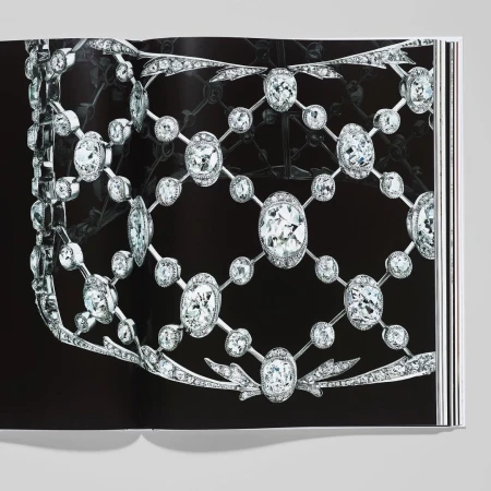 Close-up studio shot of a book open to a page featuring an elaborate diamond necklace and jewelry piece against a black background.