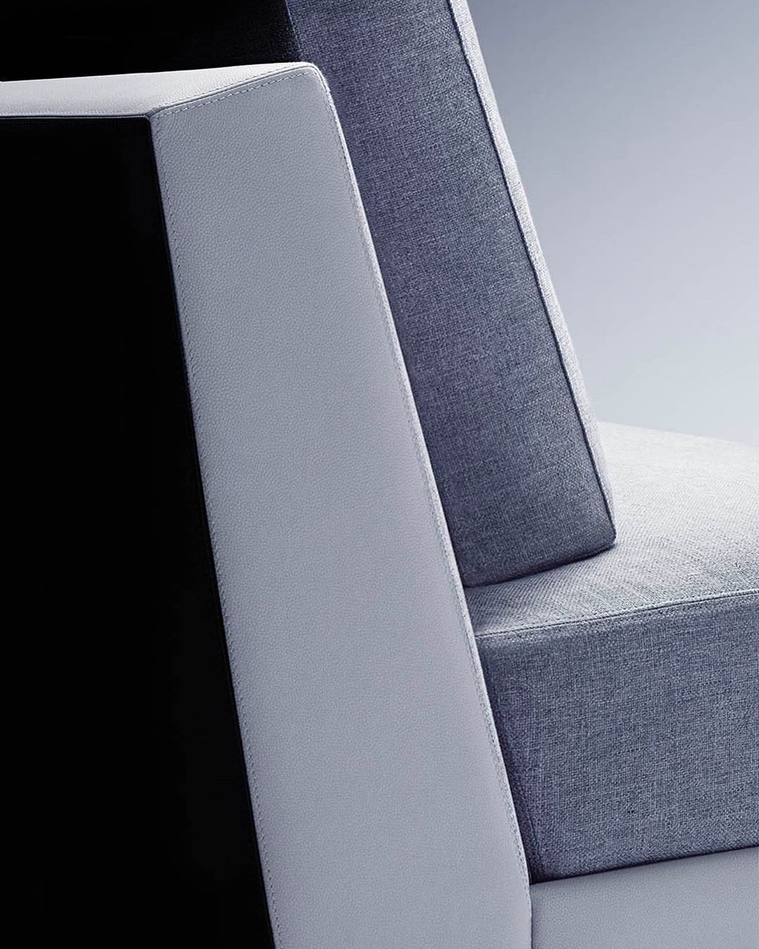 Close-up of a modern sofa featuring a gray fabric cushion, a light gray armrest, and a black panel, all against a neutral background.