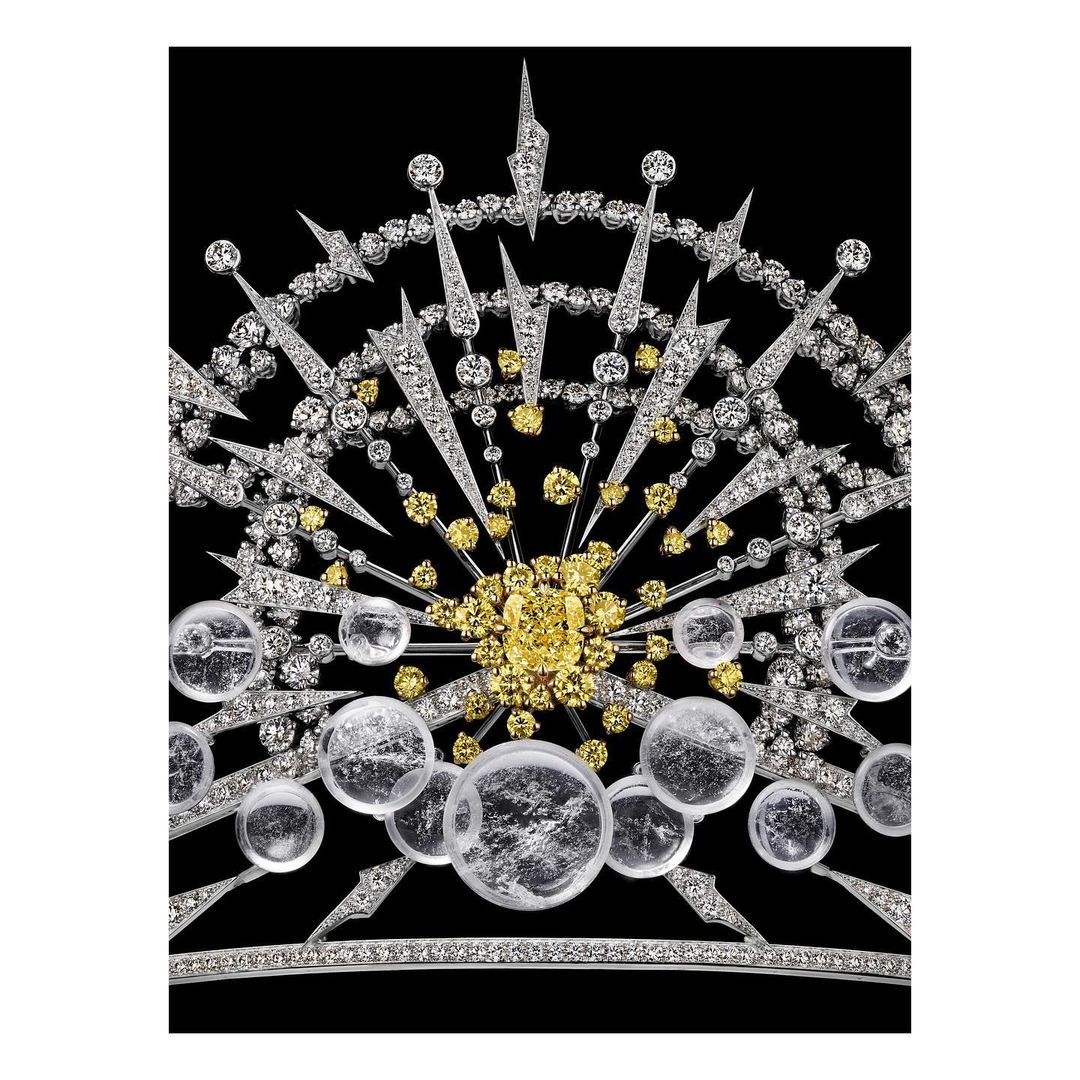 Elaborate diamond tiara featuring white and yellow diamonds in a radial starburst design, set against a stark black background.