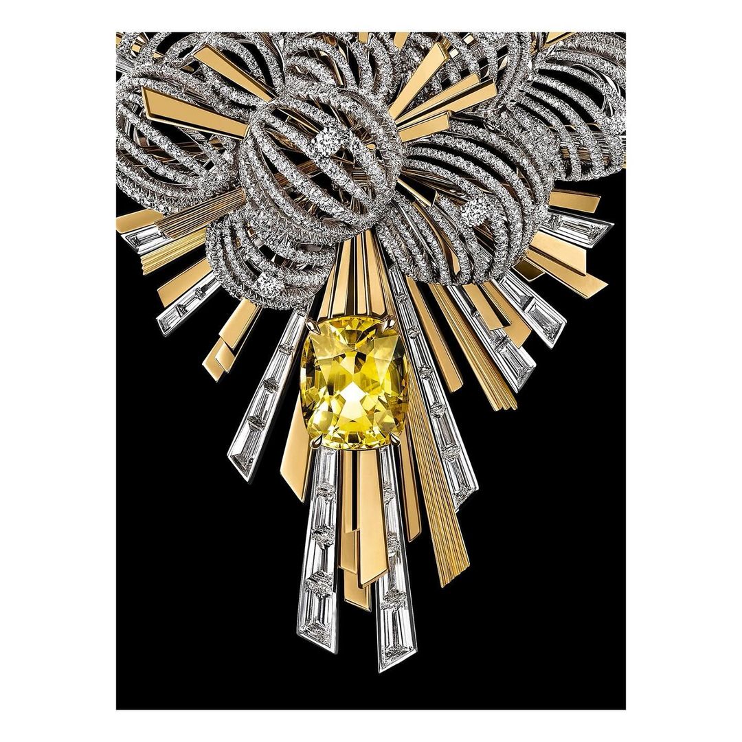 Close-up of an intricate jewelry piece featuring a large yellow gemstone surrounded by diamonds and gold, set against a black backdrop.