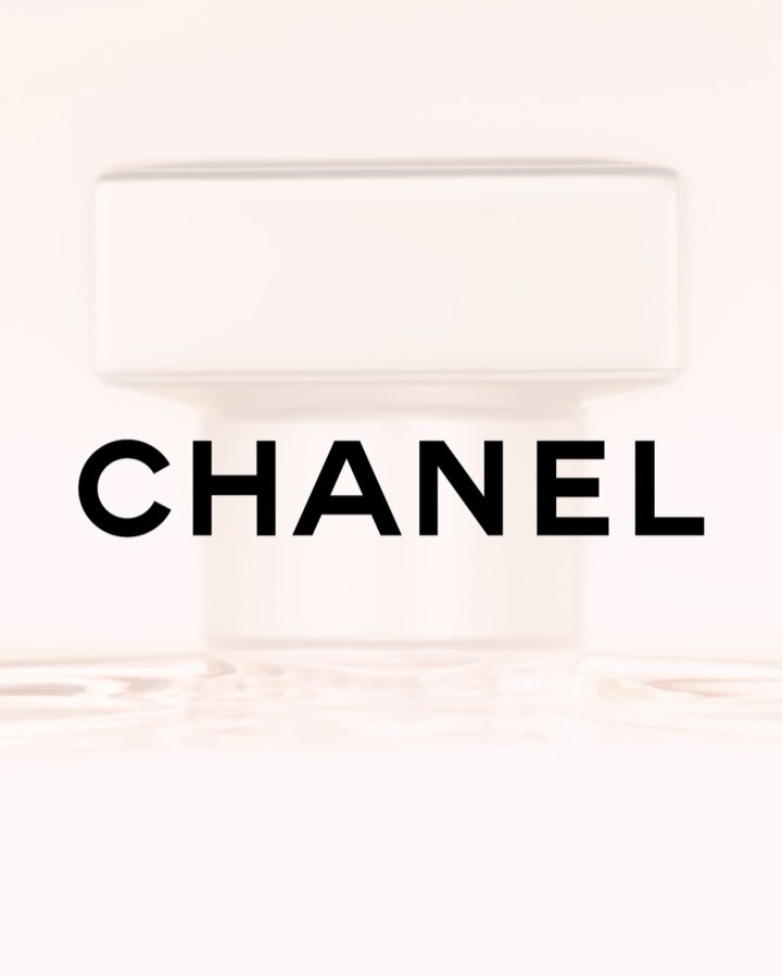 Close-up of a CHANEL perfume bottle with a white cap against a soft pink background, highlighting its simple, elegant design and branding.