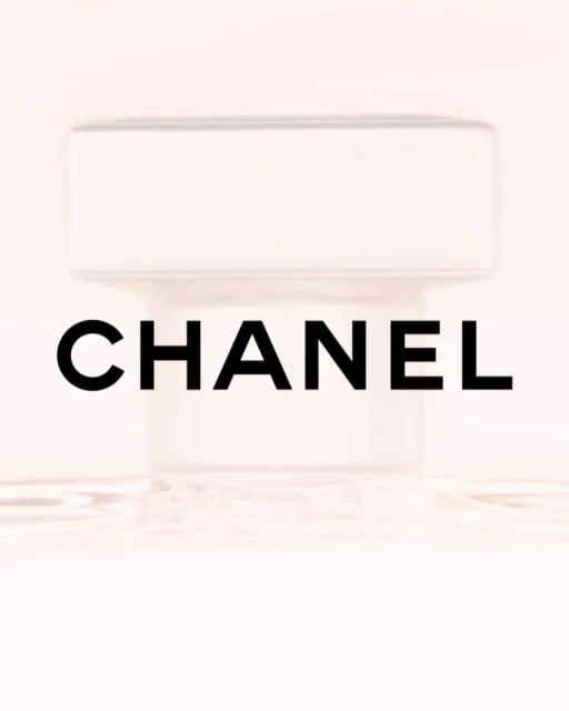 Close-up of a CHANEL perfume bottle with a white cap against a soft pink background, highlighting its simple, elegant design and branding.