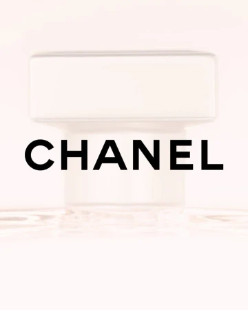 Close-up of a CHANEL perfume bottle with a white cap against a soft pink background, highlighting its simple, elegant design and branding.