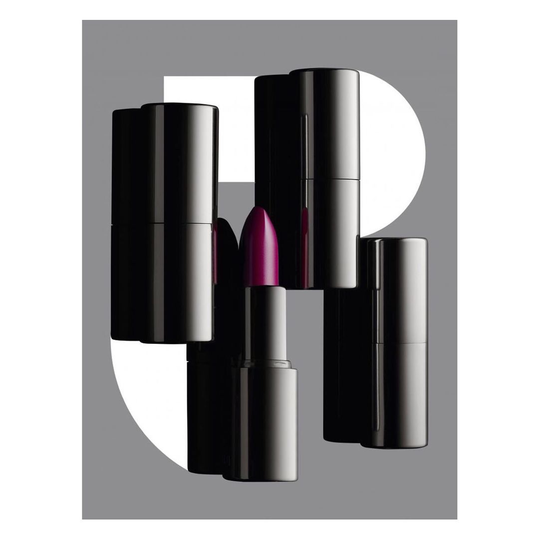 Close-up product photography of black lipstick tubes with one open tube showing purple lipstick, set against a grey graphic background.