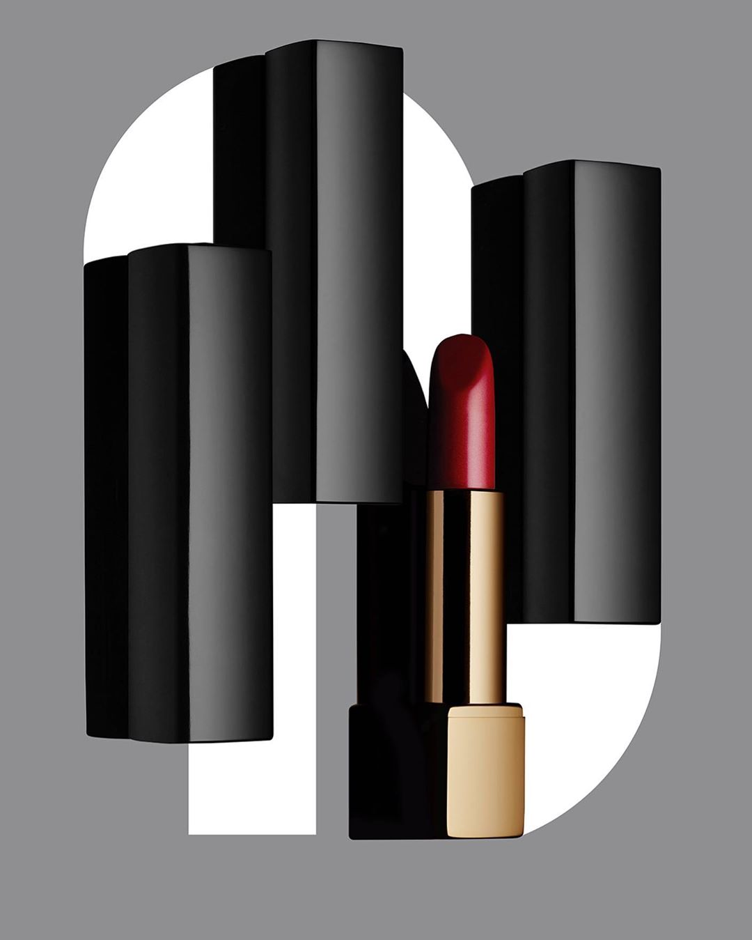 Close-up of red lipstick with black and white geometric accents on a gray background. Cosmetics advertising, beauty product.