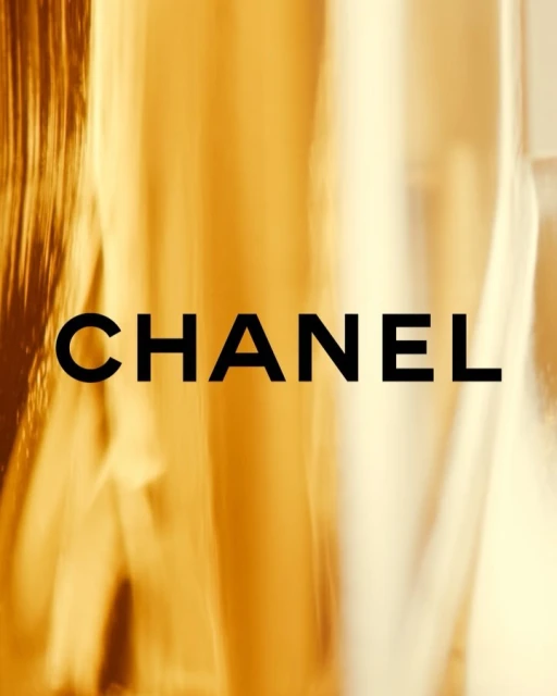 Promotional image featuring the word CHANEL in black set against an abstract, golden, blurred background, with focus on brand name.