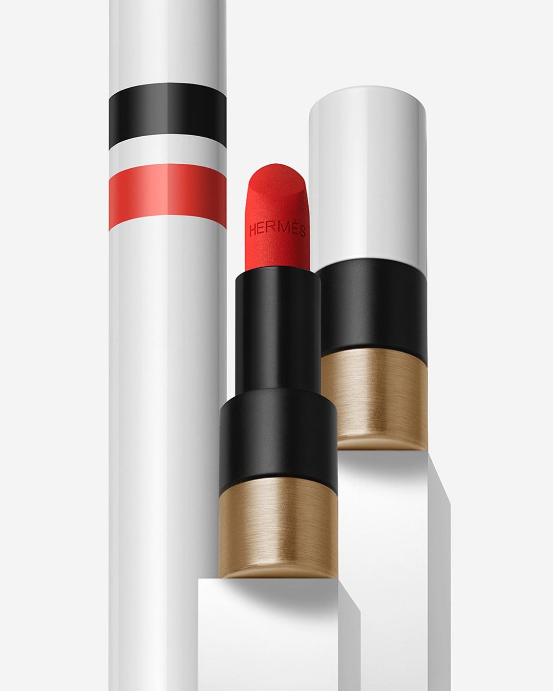 Hermes lipstick tubes in a white setting with a close-up view of a vibrant red lipstick. The lipstick tube features white, black, and gold accents.