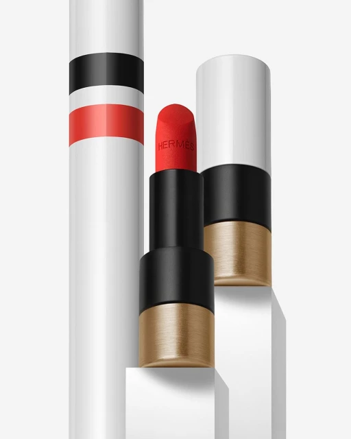 Hermes lipstick tubes in a white setting with a close-up view of a vibrant red lipstick. The lipstick tube features white, black, and gold accents.