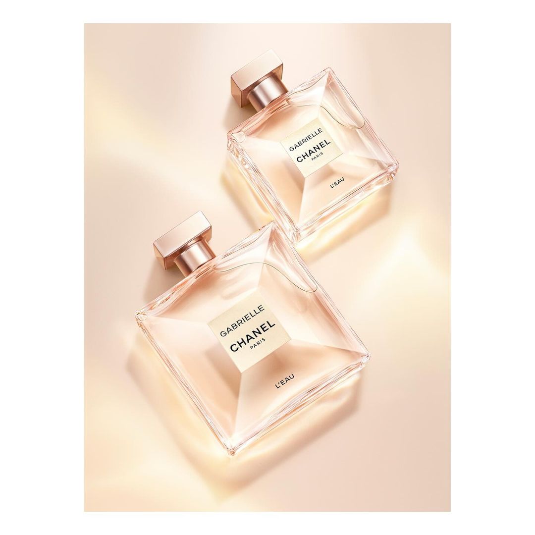 Two "Gabrielle Chanel" perfume bottles on a beige background. The perfume bottles are arranged diagonally and tilted against each other.