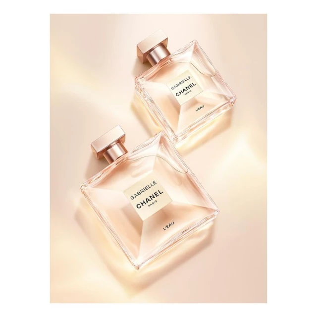 Two "Gabrielle Chanel" perfume bottles on a beige background. The perfume bottles are arranged diagonally and tilted against each other.