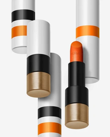 Close-up product photography of an open orange lipstick tube surrounded by floating white and black capped tubes on white background.