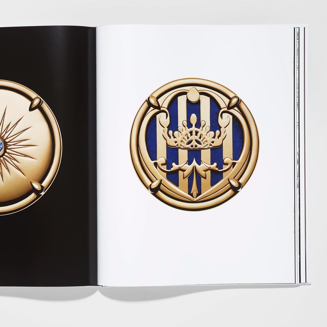 Open book displays an ornate golden medallion with a crown emblem on the right page set against a white background.
