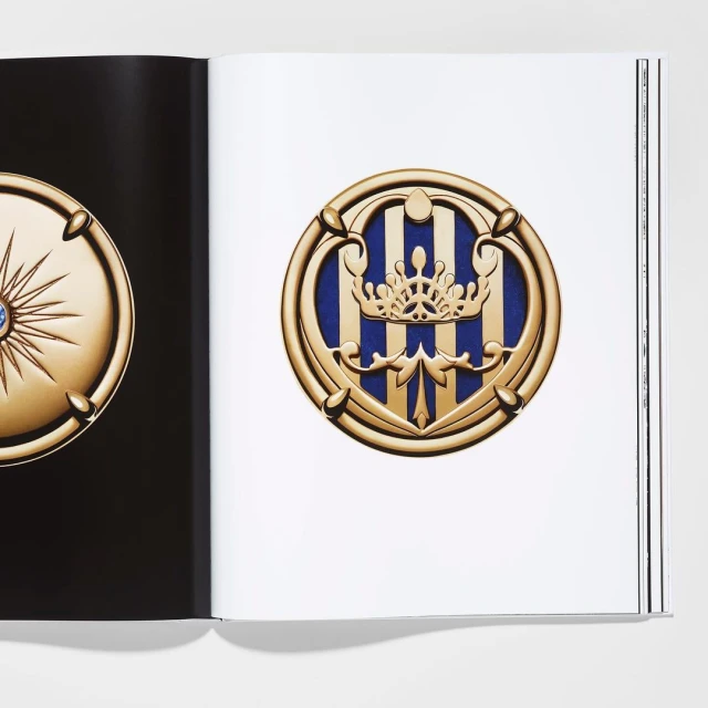 Open book displays an ornate golden medallion with a crown emblem on the right page set against a white background.
