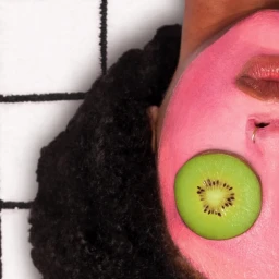 Close-up portrait of person with pink face mask and sliced kiwi on eye by Sky Pie Studio