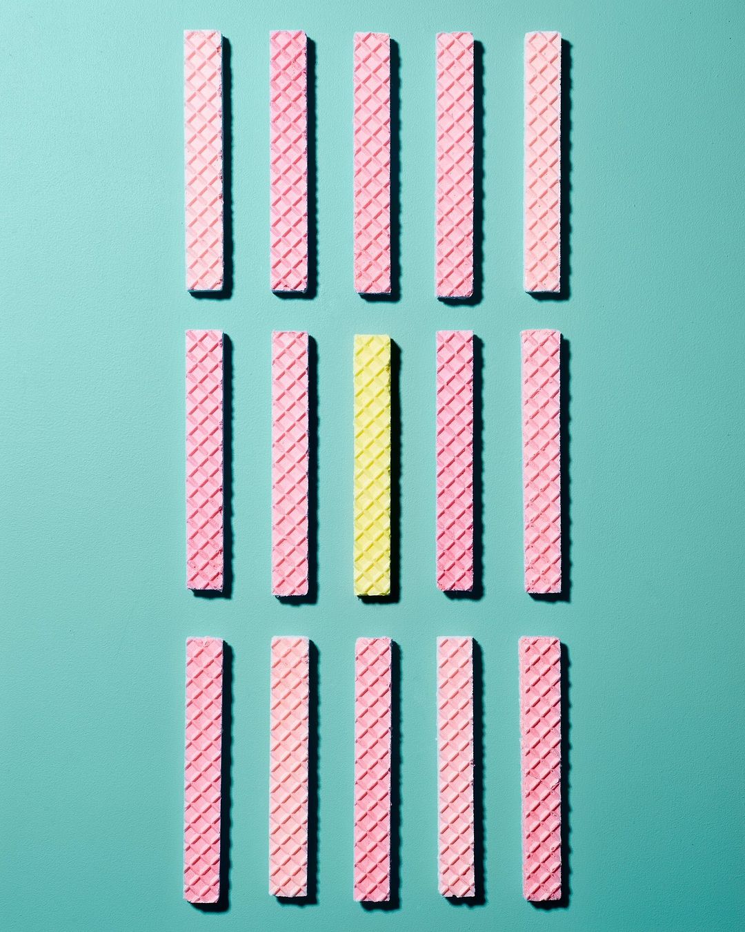 Overhead shot of arranged rows of pink and yellow wafer cookies on an aqua background, creating a simple geometric food pattern.
