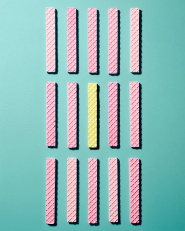 Overhead shot of arranged rows of pink and yellow wafer cookies on an aqua background, creating a simple geometric food pattern.