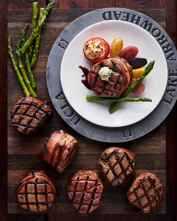 Overhead shot of grilled steak medallions with asparagus and potatoes, artfully arranged on a wooden board and decorative plate.