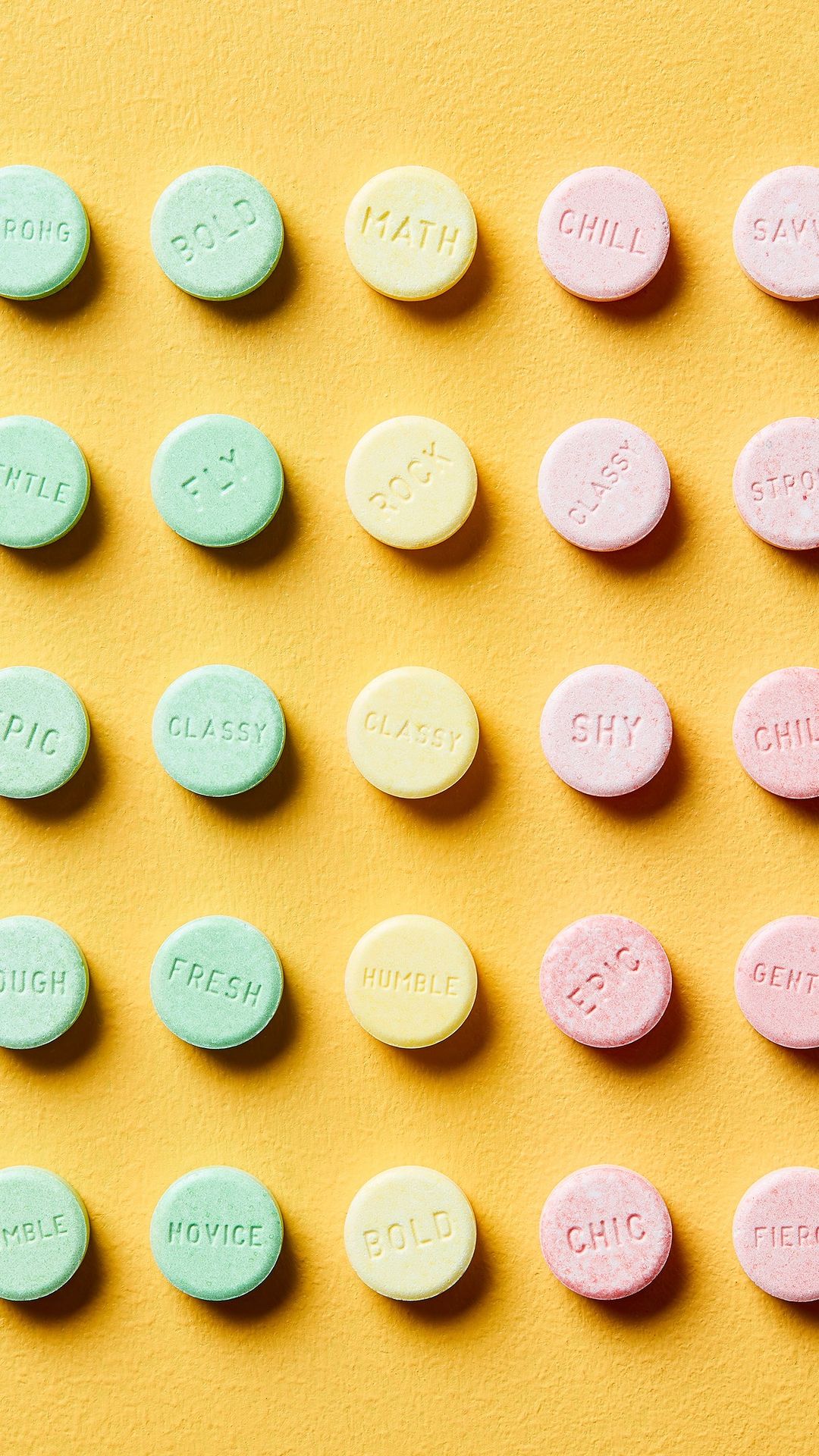 Overhead shot of pastel mint candies with positive affirmations on yellow background, arranged in grid-like rows and columns.