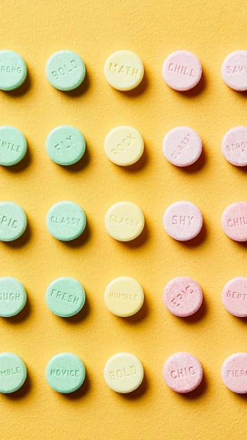 Overhead shot of pastel mint candies with positive affirmations on yellow background, arranged in grid-like rows and columns.
