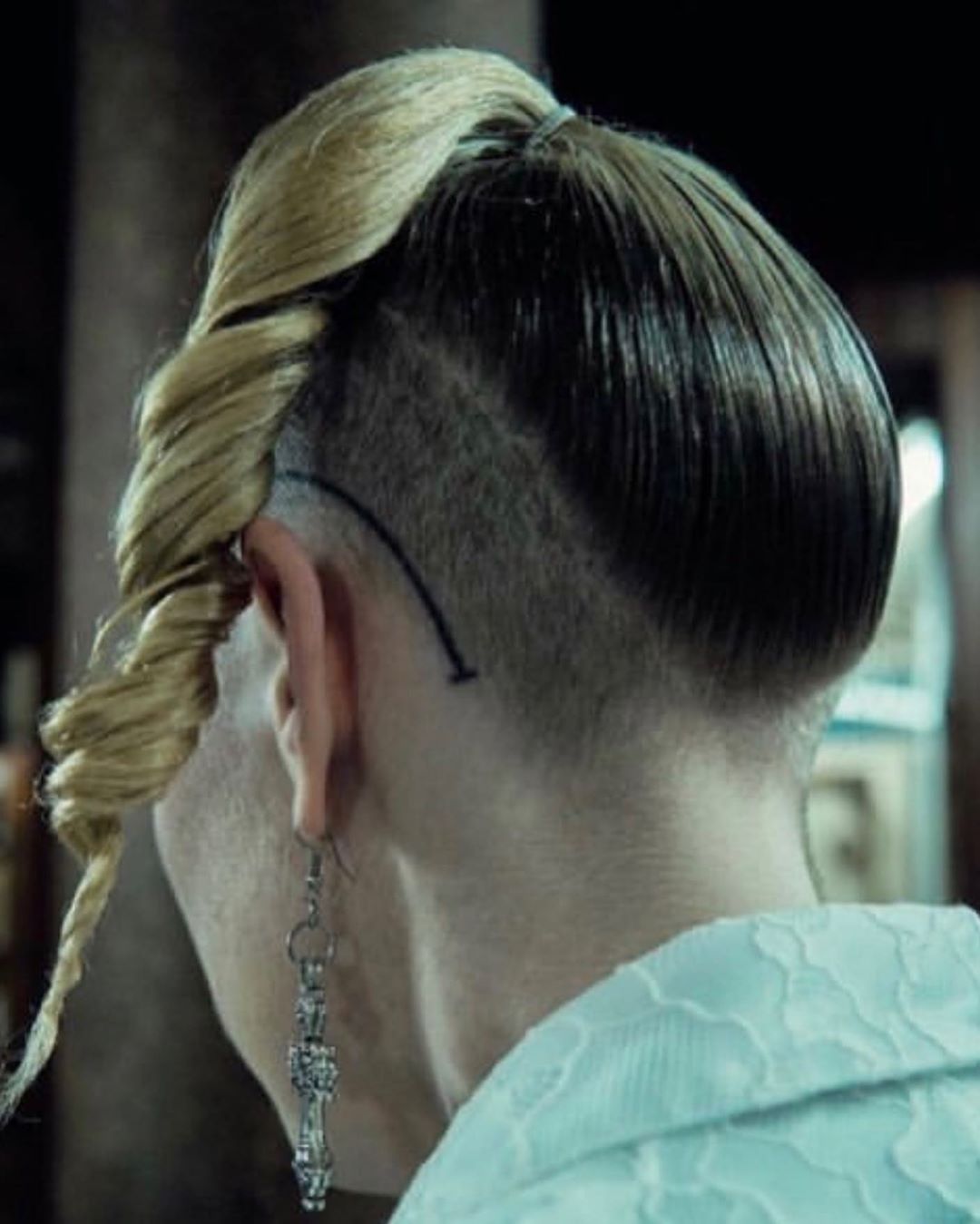 Close-up of an adult female's unique hairstyle featuring blonde twist and shaved section, accessorized with a dangling earring.