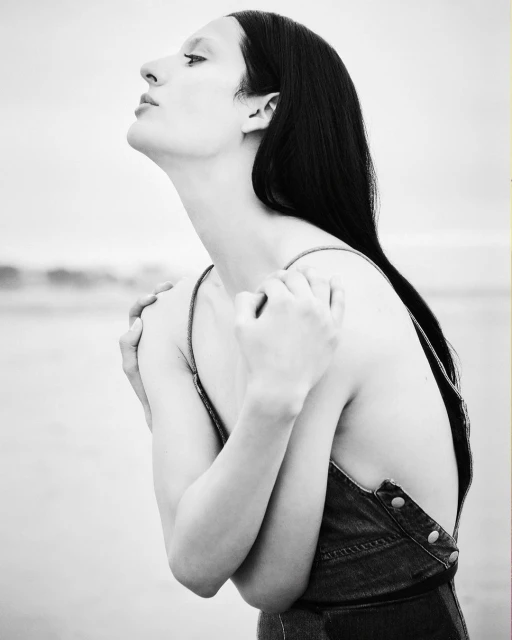 Black and white portrait of a woman with dark hair against a bright backdrop. She is facing left, arms crossed, and wearing denim.