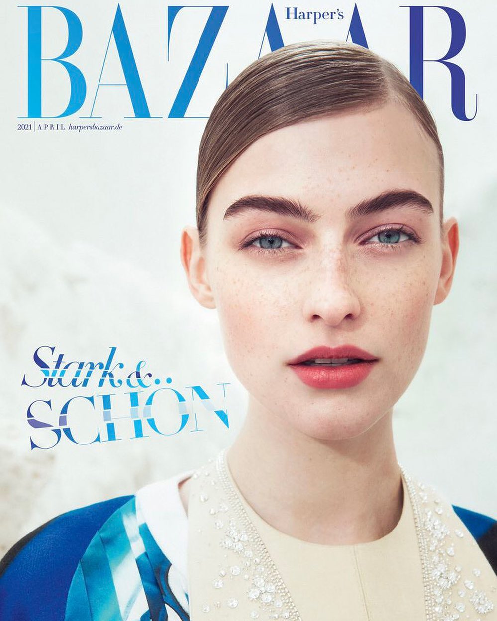 Magazine cover featuring a close-up portrait of a young, fair-skinned woman with light blue eyes and slicked-back hair, set against a soft, light backdrop.