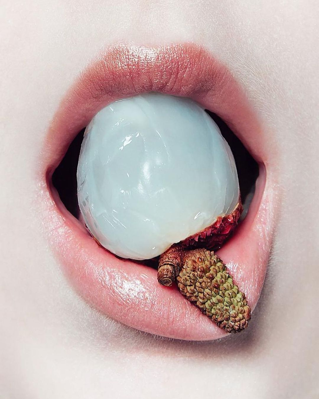 Close-up portrait of a person with a lychee in their mouth, showcasing the fruit's texture and the person's lips.