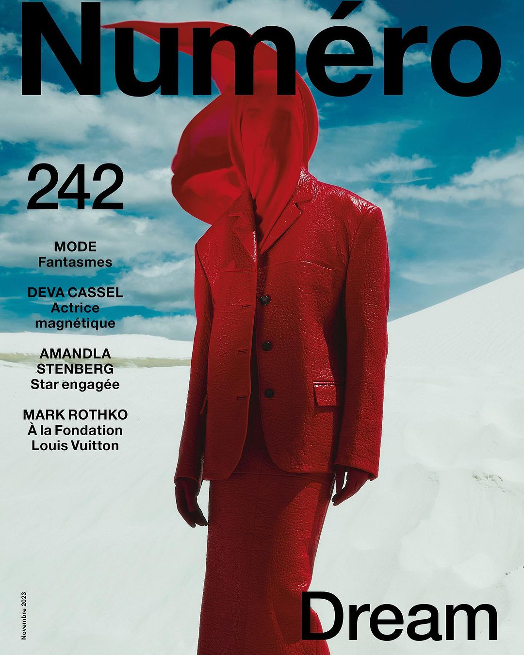 Model wearing a bright red matching suit and head covering standing against a white sand dune landscape and blue sky background