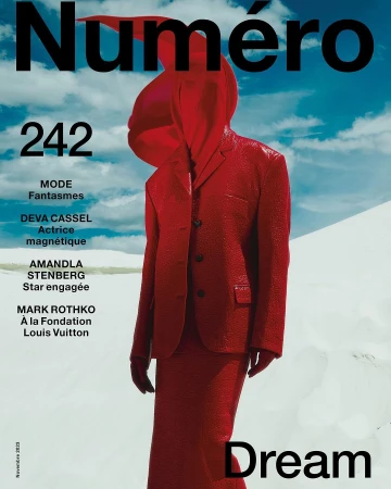 Model wearing a bright red matching suit and head covering standing against a white sand dune landscape and blue sky background
