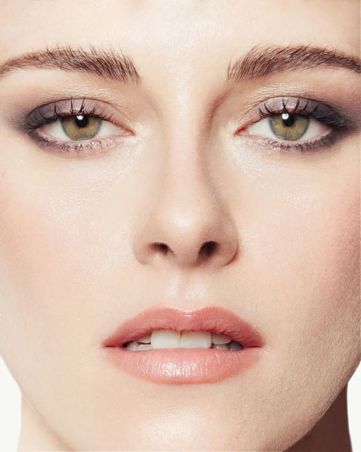 Close-up portrait of a young woman's face with smokey eye makeup, pink lips, and fair skin against a clean, white background in a beauty shot.
