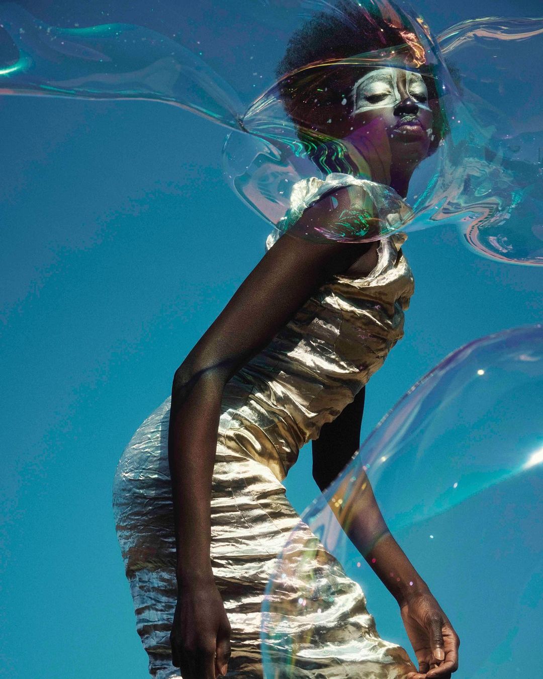 A captivating portrait showcasing a Black female model with elaborate makeup, posed against a bright blue sky with translucent bubbles.