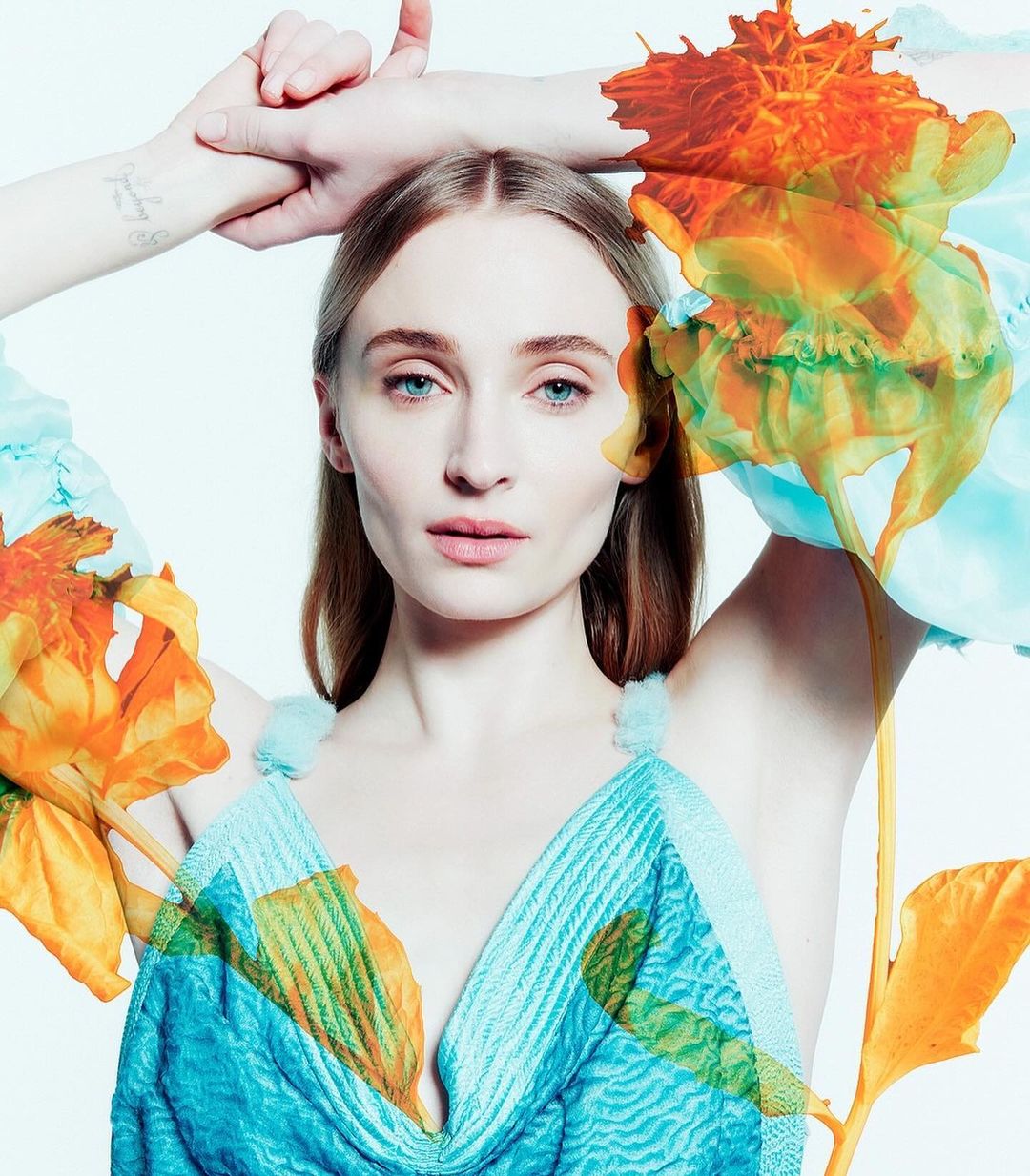 Close-up fashion portrait of a fair-skinned woman with light hair, wearing a blue top, with a floral overlay against a white background.