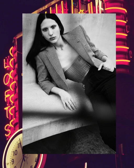 Fashion photo featuring a female model in a blazer and bustier posing in a stylish indoor setting with a neon sign and clock.
