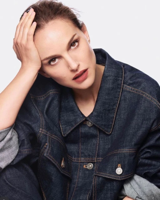 Portrait of a woman with dark hair in a denim jacket against a white background, looking directly at the camera with a neutral expression.