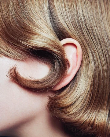 Macro close-up of glossy blonde hair styled in a wave around an ear, photographed by Sofia Sanchez and Mauro Mongiello.