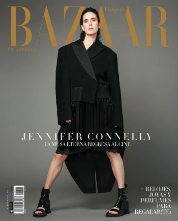 Jennifer Connelly wearing an oversized black blazer and heeled boots against a solid grey background for a magazine cover.