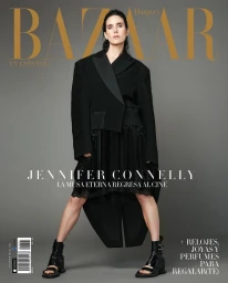Jennifer Connelly wearing an oversized black blazer and heeled boots against a solid grey background for a magazine cover.