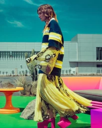 Model in yellow pleated skirt and striped shirt wearing bright pink platform heels outdoors