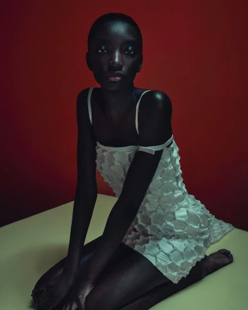 Black woman wearing a textured white mini dress kneeling against a red backdrop