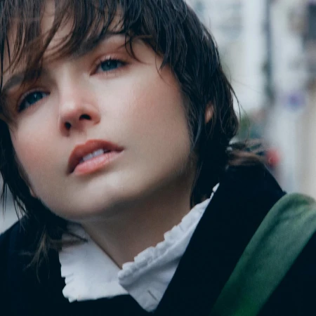 Close-up portrait of a woman with dark messy hair wearing a white ruffled collar and dark top photographed by Soliou Ligali in Paris.