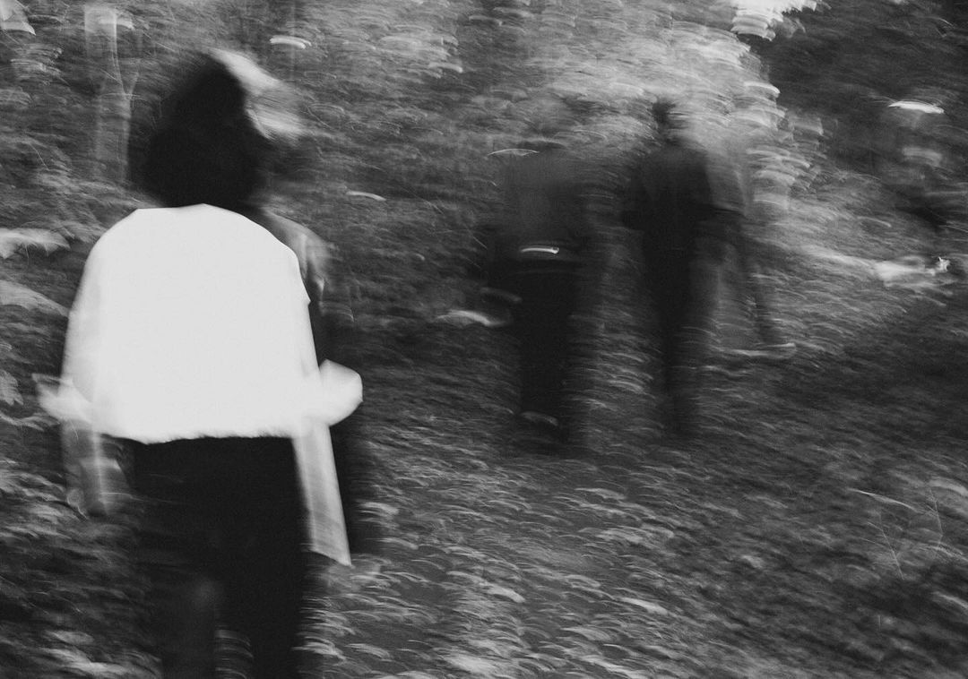 Monochrome blurred view of a group of people walking through a wooded area, creating a sense of movement and anonymity in the landscape.