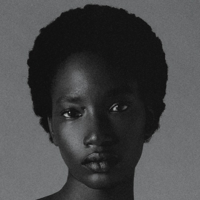 Close-up portrait of an African-American woman with dark hair, looking directly at the camera against a light gray background.