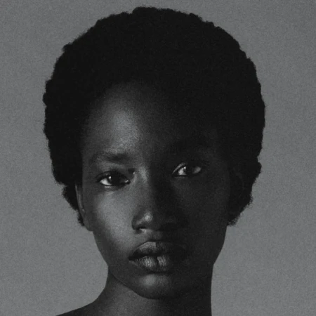 Close-up portrait of an African-American woman with dark hair, looking directly at the camera against a light gray background.