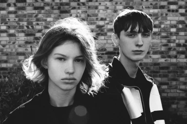 Black and white portrait of a young woman and man standing outdoors against a brick wall by photographer Soliou Ligali
