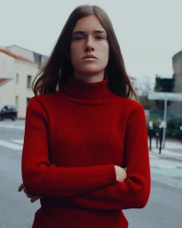 Young woman in a red turtleneck sweater standing outdoors on a street with arms crossed, photographed by Soliou Ligali in Paris.