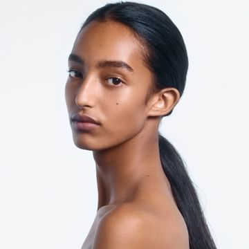Close-up portrait of an adult woman with dark hair pulled back in a ponytail, gazing intently at the camera against a white background.